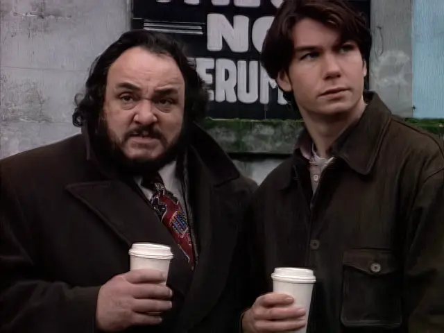 Professor Arturo and Quinn standing on a street corner drinking coffee