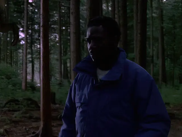 Actor Cleavant Derricks standing in a British Columbia forest at dusk in the episode In Dino Veritas