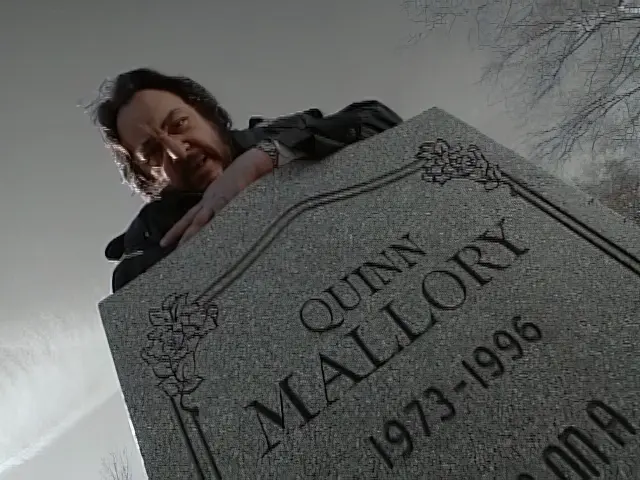 Professor Arturo standing behind Quinn Mallory's tombstone in the Sliders episode Into the Mystic